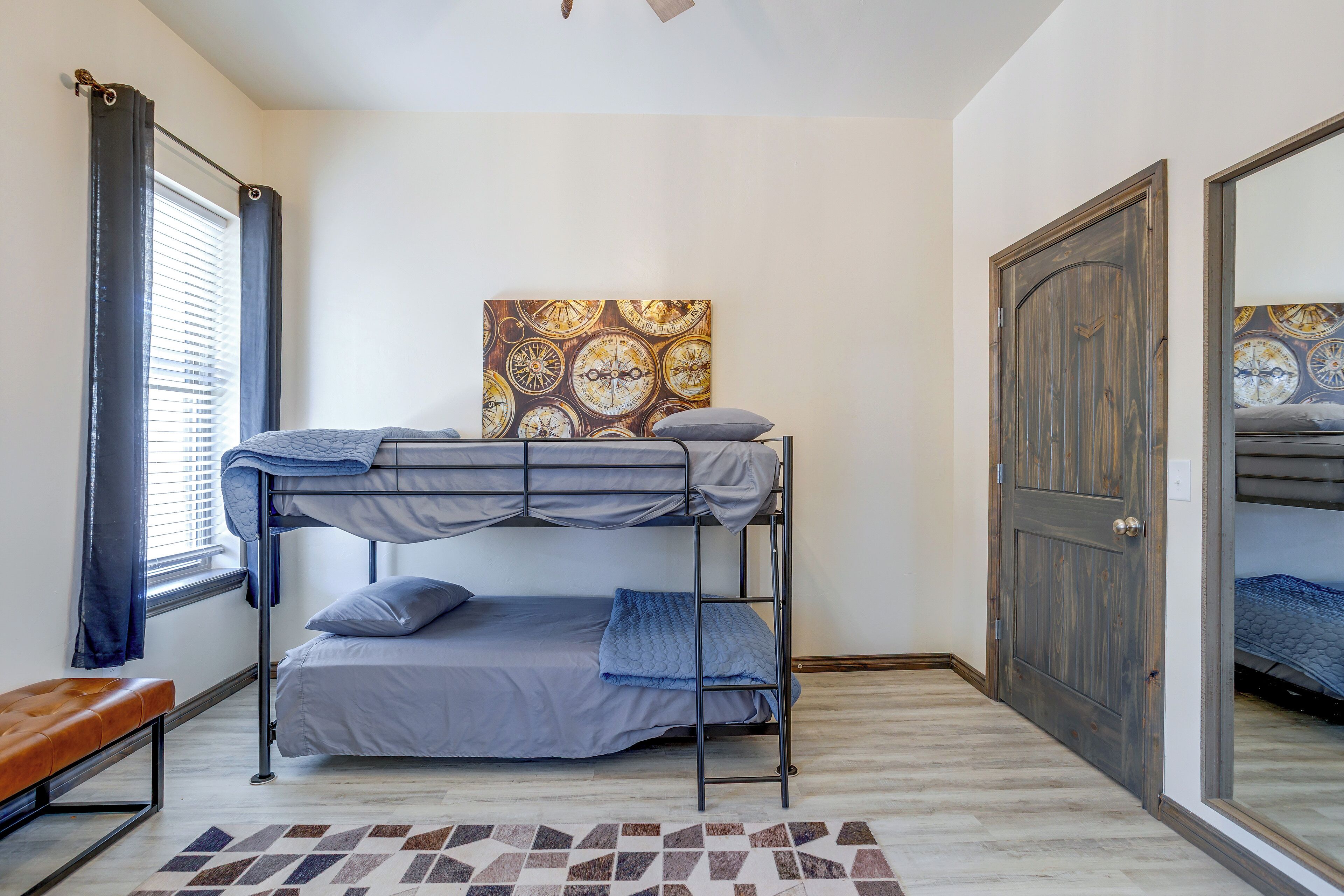 Une chambre avec un lit superposé, un mur décoré d’un motif, une fenêtre avec des rideaux et une porte en bois.