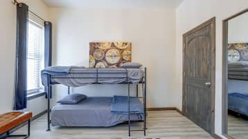 Une chambre avec un lit superposé, un mur décoré d’un motif, une fenêtre avec des rideaux et une porte en bois.
