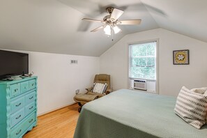 Un dormitorio con cama, una silla, cómoda, ventilador de techo, ventana con persianas y aire acondicionado instalado en la pared.