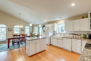 A spacious kitchen with white cabinetry, a dining area with wooden chairs, and a large island with a granite countertop. - 3 Mi to Assateague Beach! Home w/ Furnished Deck (Chincoteague)