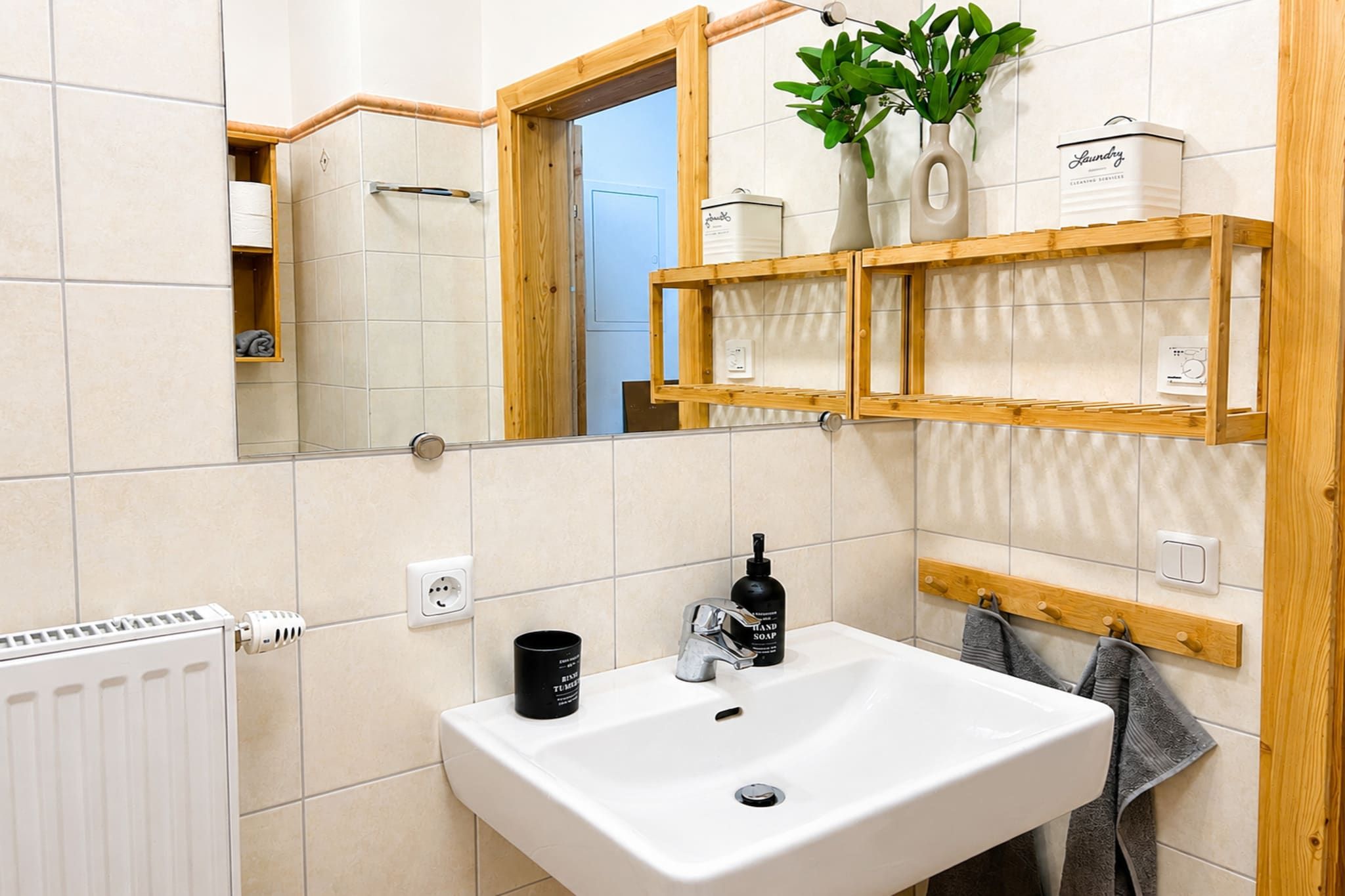 A bathroom with a white sink, a mirror, a towel rack, and a shelf with toiletries.