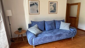 Ein blaues Sofa mit Kissen, ein kleiner runder Holztisch mit einer Pflanze und zwei gerahmte Bilder an der Wand.