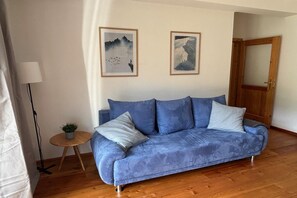 A blue sofa with cushions, a small round wooden table with a plant, and two framed pictures on the wall. - Apartment on the ski slope (Bad Kleinkirchheim)