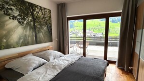 Ein Schlafzimmer mit einem großen Bett, Blick auf eine grüne Landschaft durch eine Schiebetür und einem Baumgemälde an der Wand.