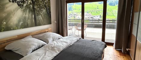 Un dormitorio con una cama grande, vista a un paisaje verde a través de una puerta corrediza y un cuadro de árboles en la pared.