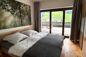 A bedroom with a large bed, a view of a green landscape through a sliding door, and a painting of trees on the wall. - Apartment on the ski slope (Bad Kleinkirchheim)