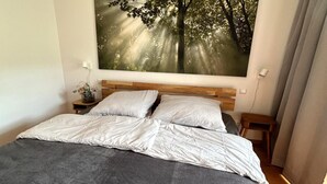 Ein Schlafzimmer mit einem Bett, einem Nachttisch, einem Wandbild und einem Fenster mit Vorhängen.