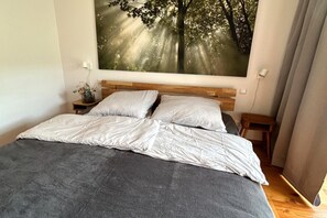 A bedroom with a bed, a nightstand, a wall-mounted painting, and a window with curtains. - Apartment on the ski slope (Bad Kleinkirchheim)