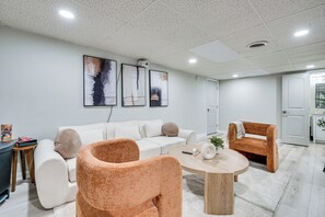 Un saló modern amb un sofà blanc, dos butaques, una taula de centre i decoració mural abstracta.