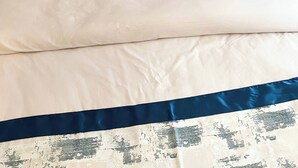 A bed with a grey upholstered headboard, white bedding, and two decorative pillows with a distressed design.