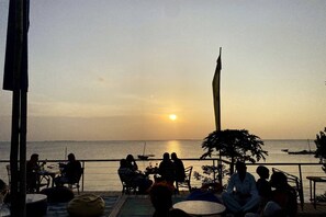 A sunset view from a terrace with people seated, overlooking the sea.