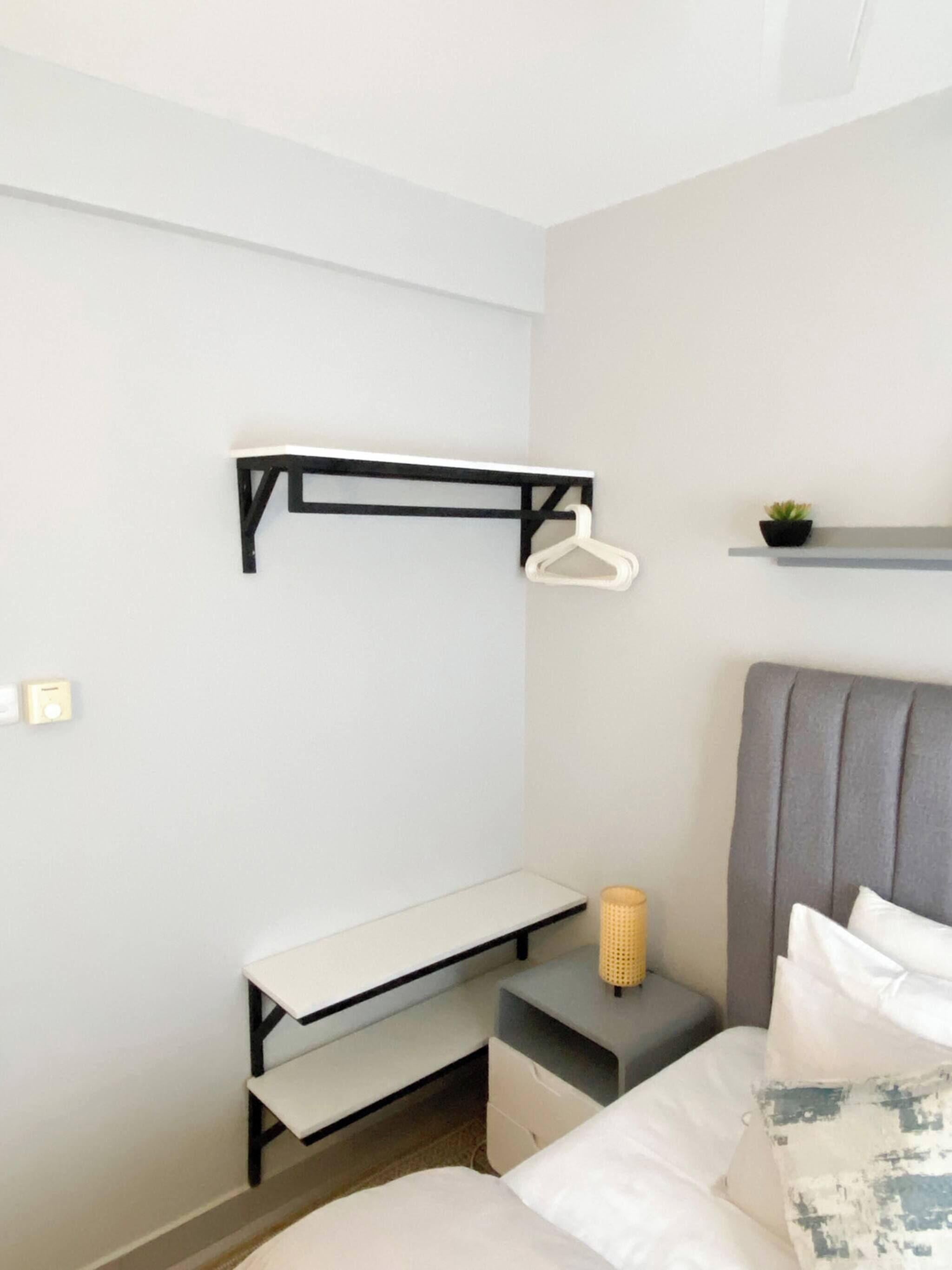 Una camera da letto con un letto, un comodino, una piccola mensola e una rastrelliera a muro con un appendiabiti.