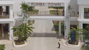 En moderne bygning med skiltage 'FUMBA TOWN', et overdækket gangareal og en person, der går forbi.