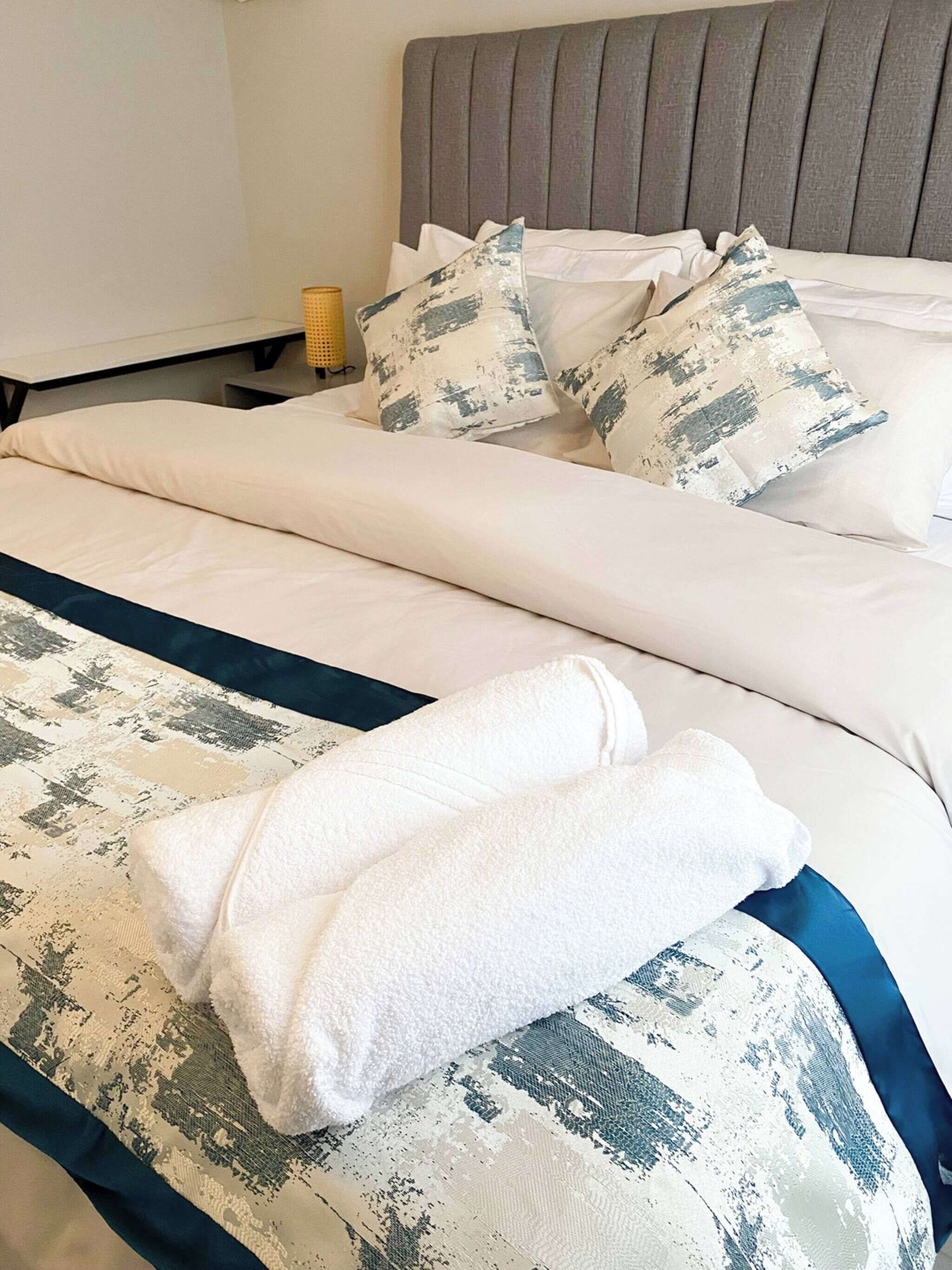 Uma cama bem arrumada com lençóis brancos e almofada estampada em azul e branco.