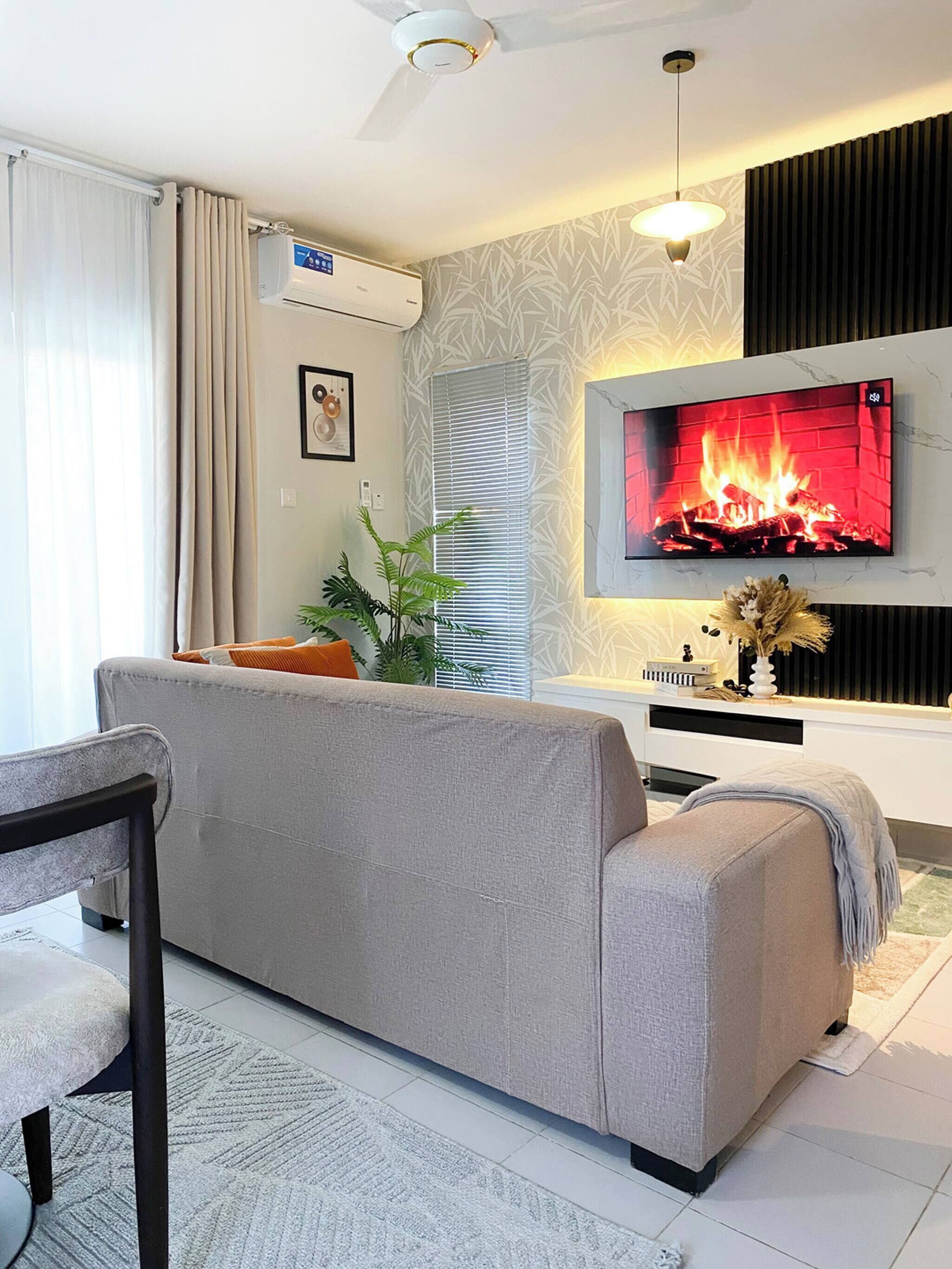 Uma sala de estar moderna com um sofá, uma televisão de tela plana na parede, um ventilador de teto e uma janela com persianas.