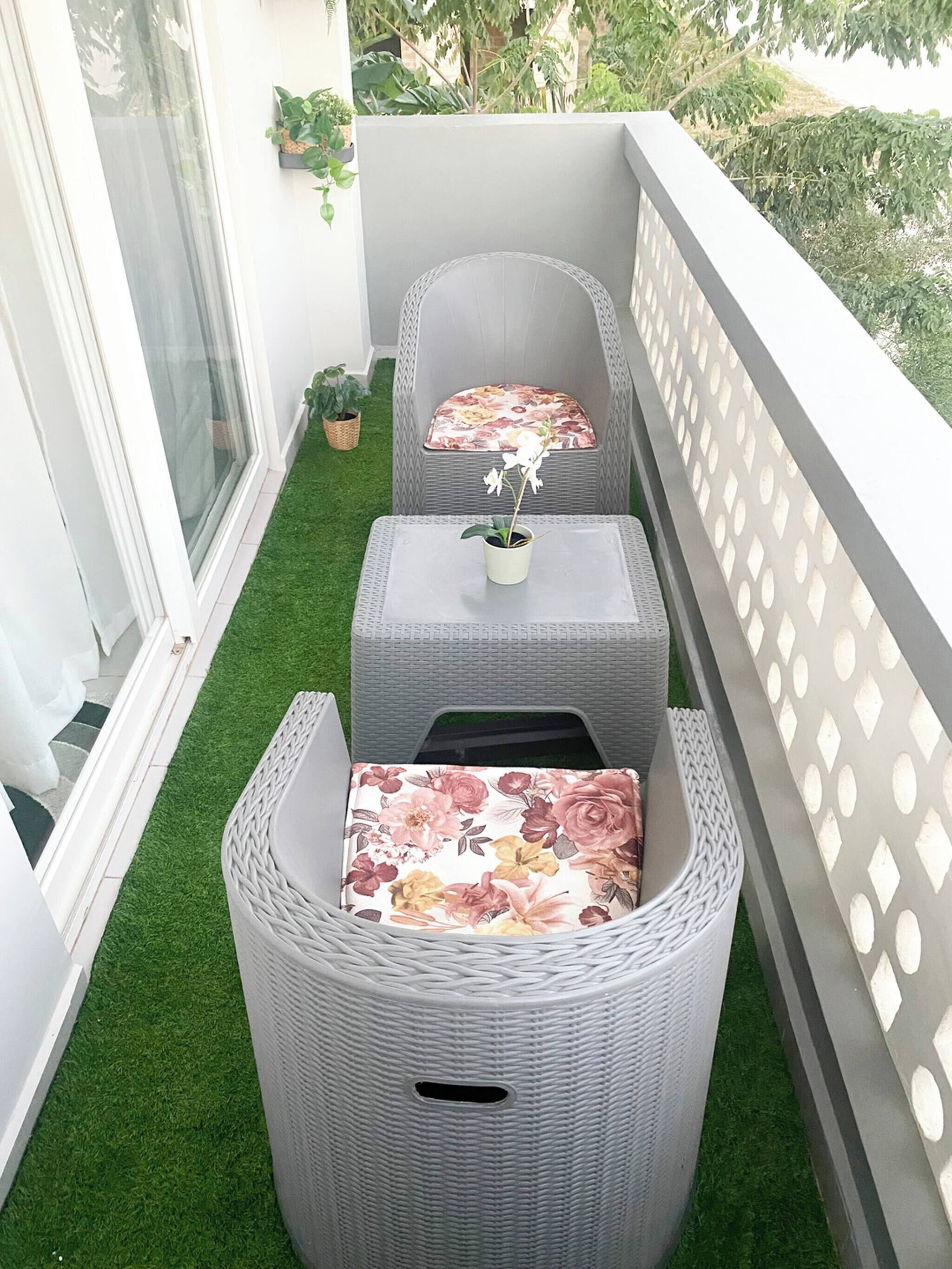 A balcony with two wicker chairs, each with a cushion, and a small table with a plant.