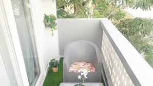 A balcony with two wicker chairs, each with a cushion, and a small table with a plant.