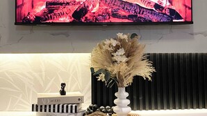A flat-screen TV mounted on a wall above a white console with a decorative vase and a book.