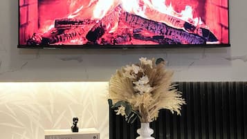 A flat-screen TV mounted on a wall above a white console with a decorative vase and a book.