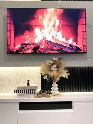 A flat-screen TV mounted on a wall above a white console with a decorative vase and a book.
