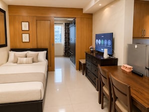A modern hotel room with a bed, a desk, a television, and a refrigerator. - Modern 2-Bedroom Apartment with Shared Pool in Central Pasay (Pasay City)