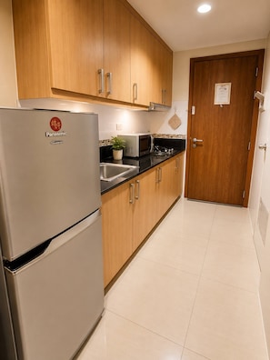 A kitchen with wooden cabinets, a stainless steel refrigerator, a microwave, and a sink. - Modern 2-Bedroom Apartment with Shared Pool in Central Pasay (Pasay City)