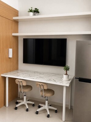 A modern kitchen with a white marble countertop, two office chairs, a flat-screen TV, a stainless steel refrigerator, and two potted plants on a shelf. - Quaint 1BR Condo Terrace-pool view front MOA-Shell (Pasay City)