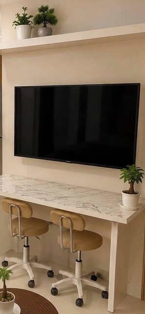 A modern kitchen with a large flat-screen TV mounted above a marble countertop, two office chairs, and potted plants. - Quaint 1BR Condo Terrace-pool view front MOA-Shell (Pasay City)