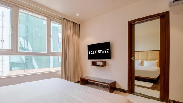 A hotel room with a bed, a television mounted on the wall, a mirror, and a window with curtains.