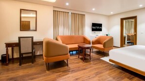 A hotel room with a bed, two armchairs, a small table, a desk, a TV, and a mirror.