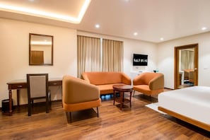 Habitación de hotel con una cama, dos sillones, una mesita, un escritorio, un televisor y un espejo.