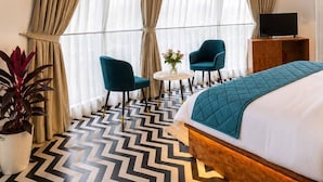 A hotel room with a bed, two chairs, a small table, a TV, curtains, and a potted plant. - The Cocoon Dhaar Chakrata (Chakrata)