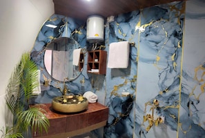 Un baño con pared de mármol, un espejo redondo, un lavamanos dorado y un perchero para toallas.