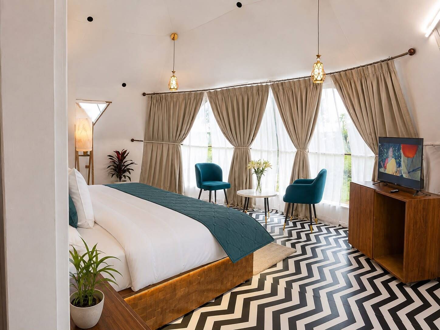 Ein Hotelzimmer mit einem Bett, zwei Stühlen, einem kleinen Tisch, einem Fernseher und einem großen Fenster mit Vorhängen.