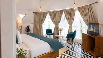 Ein Hotelzimmer mit einem Bett, zwei Stühlen, einem kleinen Tisch, einem Fernseher und einem großen Fenster mit Vorhängen.