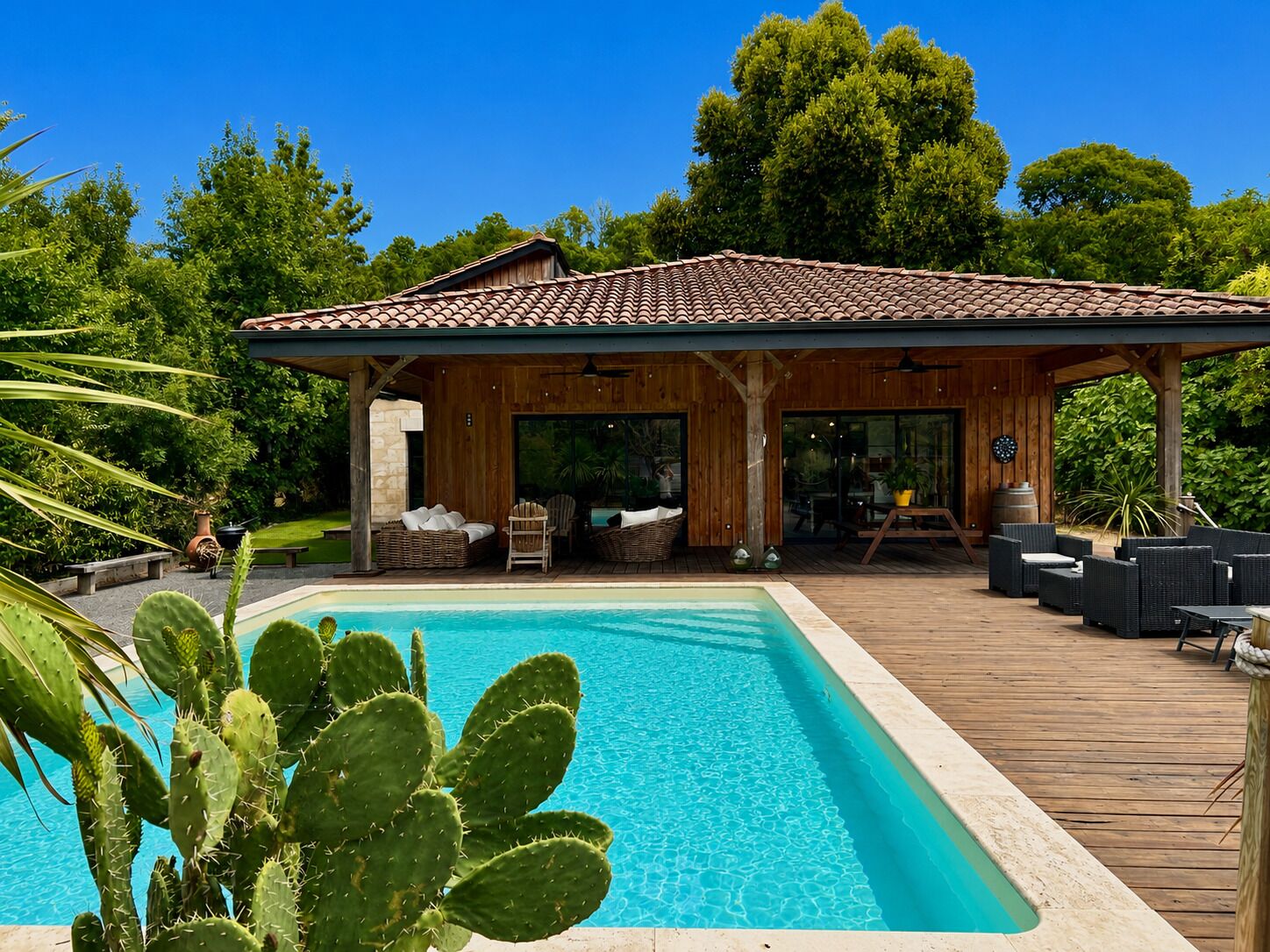 A wooden deck with a pool, outdoor seating, and a covered area with a tiled roof.