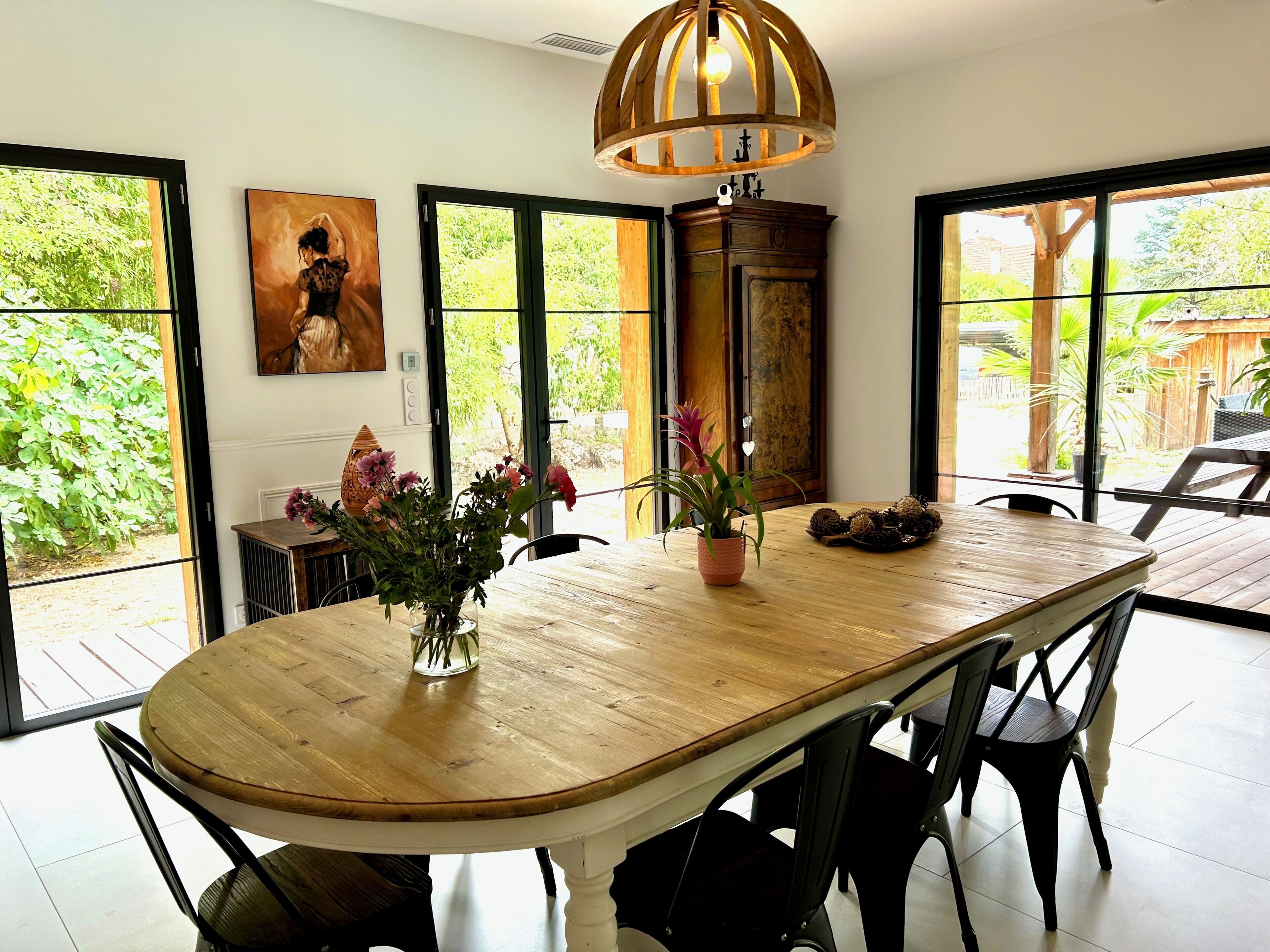 A dining area with a wooden table, chairs, a vase with flowers, and a pendant light.