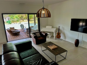 A modern living room with a leather sofa, a coffee table, a piano, a guitar, and a TV. - Villa with pool, sleeps 8, 4,500 m² garden, Bordeaux (Latresne)