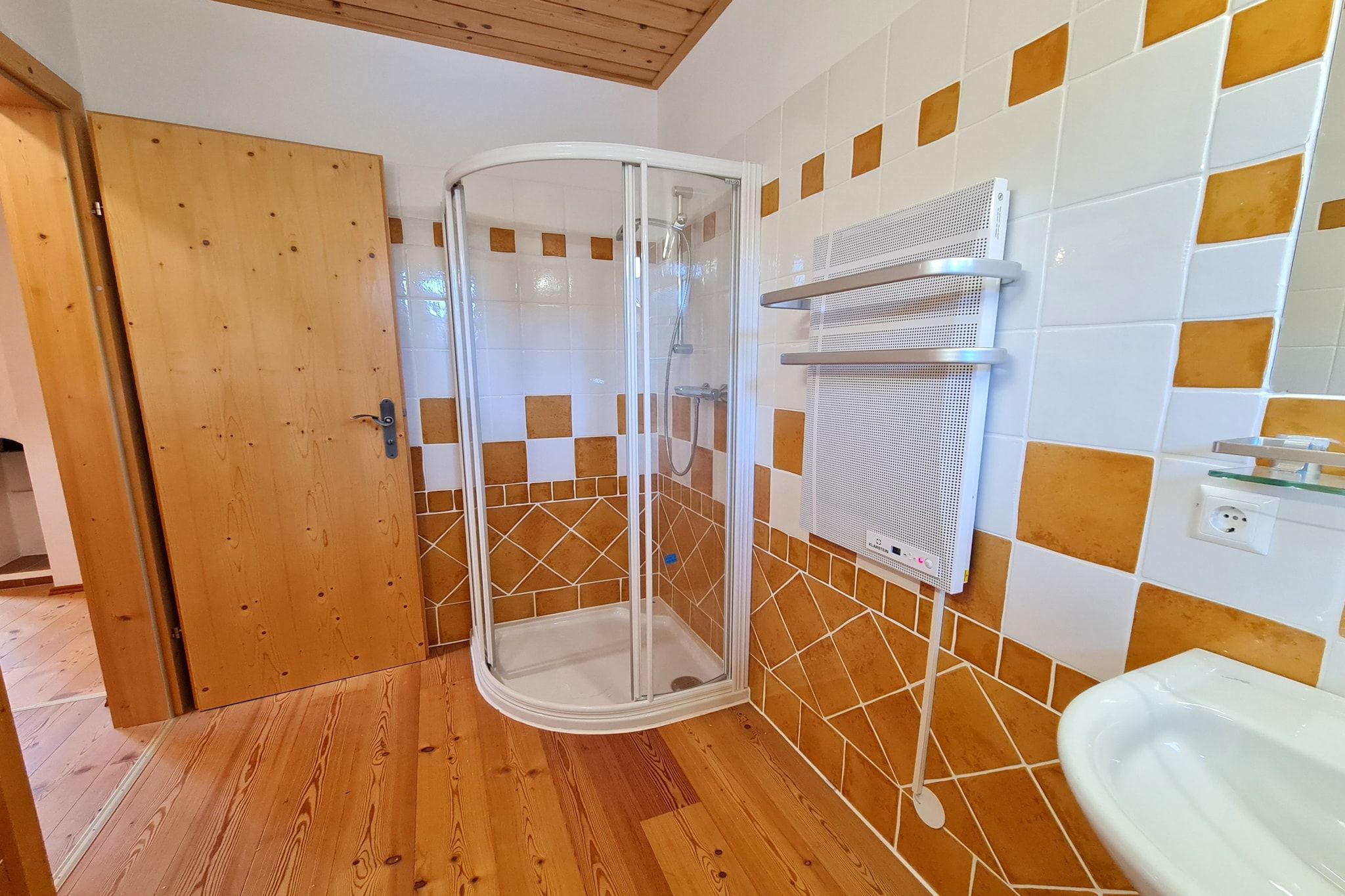 Ein Badezimmer mit Dusche, gefliesten Wänden, Holzboden und Waschbecken in Weiß.