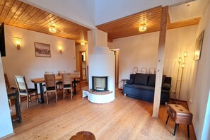 A cozy living room with a fireplace, wooden flooring, and a dining area with chairs and a table. - Modern apartment in Bad Kleinkirchheim (Bad Kleinkirchheim)