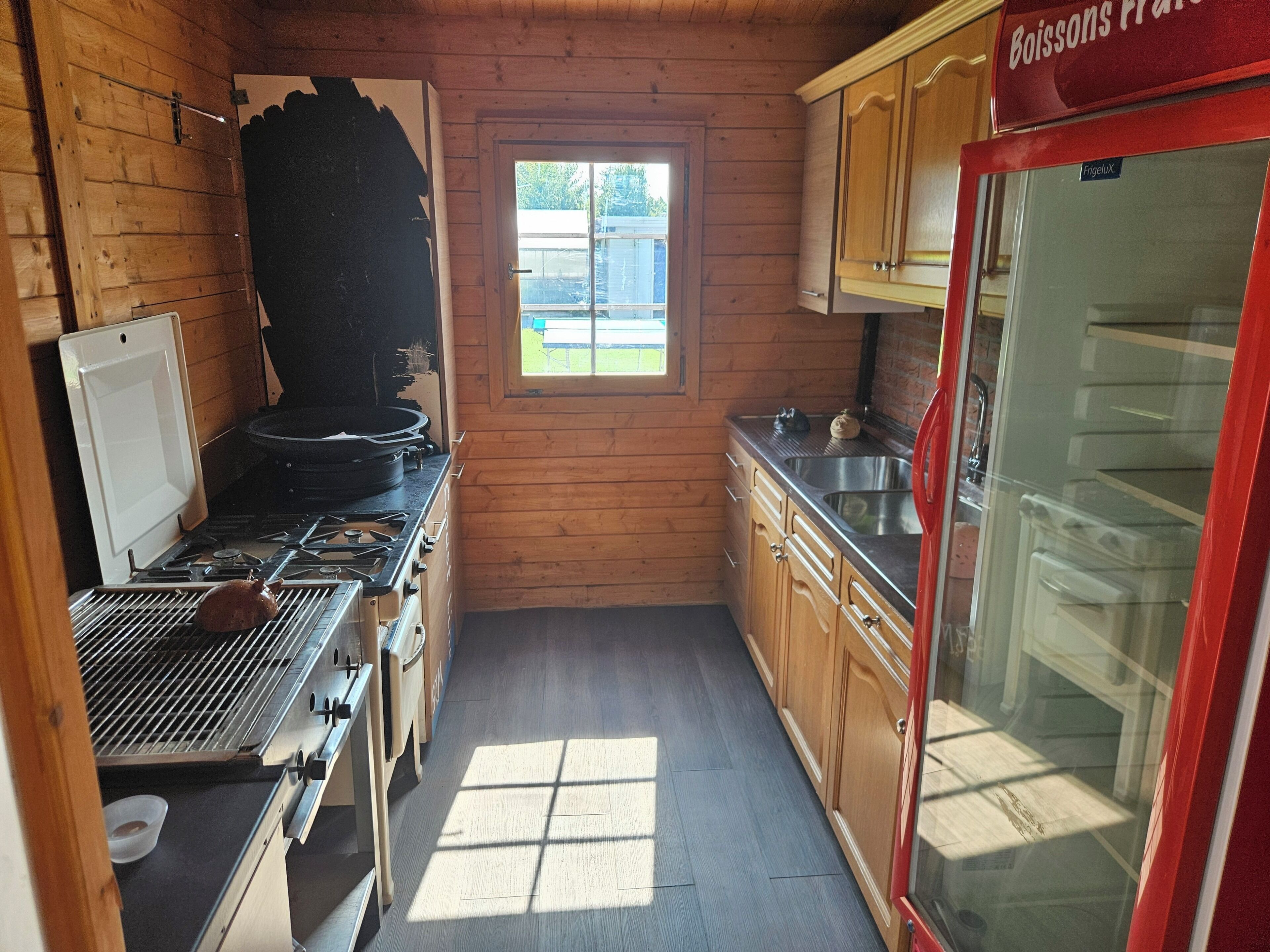 Een kleine keuken met houten wanden, een raam, een fornuis en een koelkast.