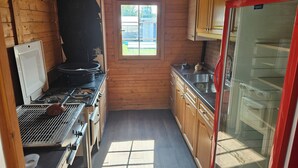 A compact kitchen with wooden walls, a window, a stove, and a refrigerator.