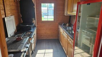 Een kleine keuken met houten wanden, een raam, een fornuis en een koelkast.