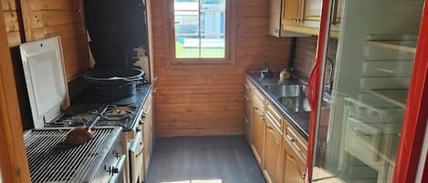 A compact kitchen with wooden walls, a window, a stove, and a refrigerator.