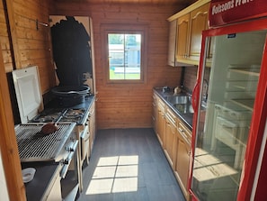 A compact kitchen with wooden walls, a window, a stove, and a refrigerator.