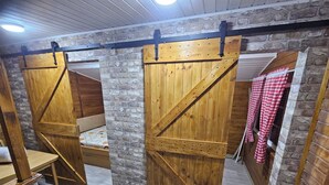 A rustic room with wooden walls and a slanted ceiling. There are two wooden beds with metal frames and a bench.