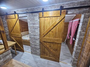 A rustic room with wooden walls and a slanted ceiling. There are two wooden beds with metal frames and a bench.