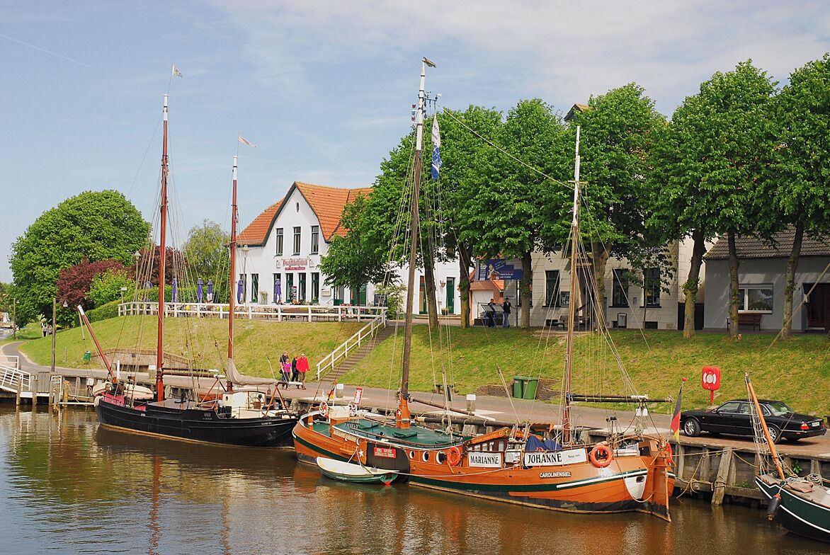 Een haven met aangemeerde boten, een wit gebouw met een rood dak, en een gazon met bomen.