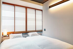 Ein Hotelzimmer mit einem Bett, einem Nachttisch, einer Lampe und einem großen Fenster mit Holzrahmen.