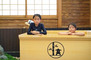 Twee kinderen zitten aan een houten tafel met een Japans symbool, in een kamer met houten wanden en een raam.